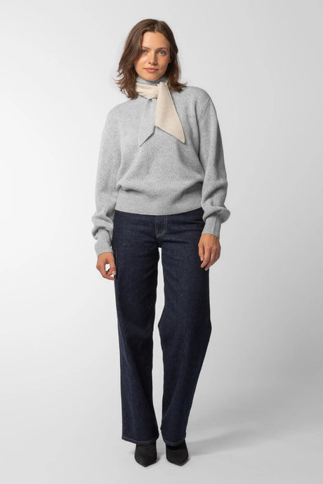 Woman wearing a light grey melange pure cashmere pointelle jumper and a white and grey soft cashmere neckerchief scarf